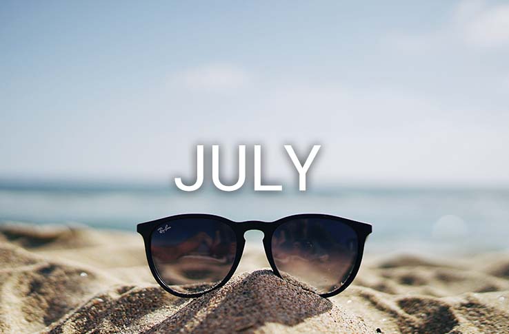 Sunglasses on a beach with the text July
